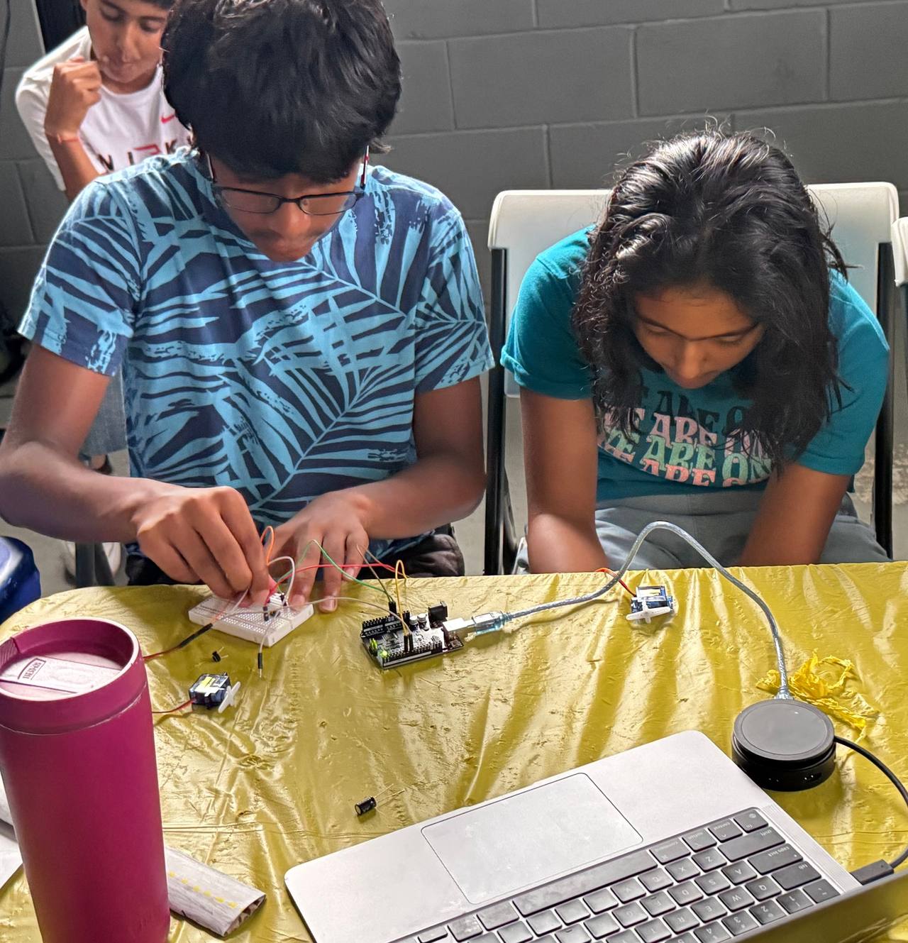 A student pushes a jumper wire into a breadboard connected to an Arduino Uno while another student watches.