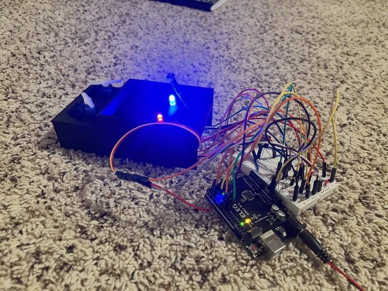 A blue 3D-printed box with a servo and glowing LEDs, wired to an Arduino-compatible board and a breadboard.